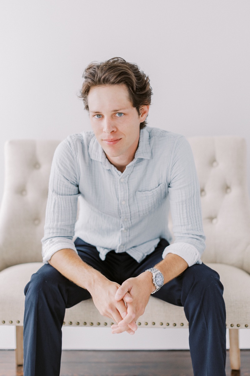 Blake seated, leaning forward with his hands together.